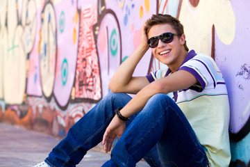 Young man sitting against graffiti wall