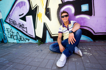 Young man sitting against graffiti wall