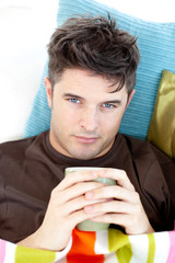 Sick man lying on a sofa holding a cup