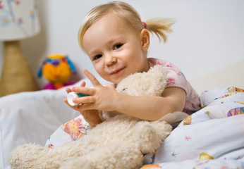 little girl in bed playing with teddy bear - obrazy, fototapety, plakaty