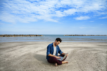 Fototapeta na wymiar Young man sitting on beach with laptop