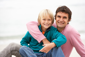 Father And Son Sitting On Winter Beach Together