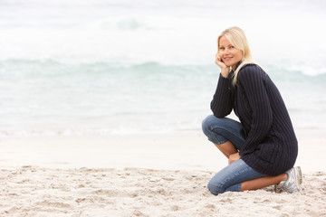 Young Woman On Holiday Kneeling On Winter Beach