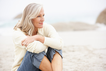 Fototapeta na wymiar Senior Woman On Holiday Sitting On Winter Beach