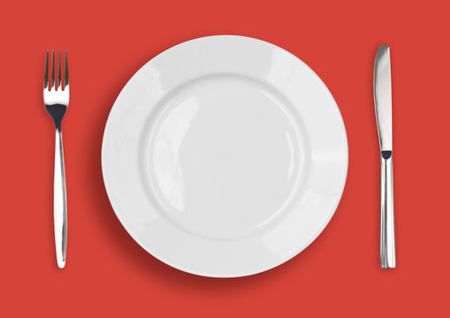 Knife, white plate and fork on red background