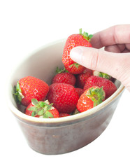 fingers removing strawberry from bowl on white