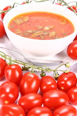Tomato soup with basil leaves with fresh tomatoes around it