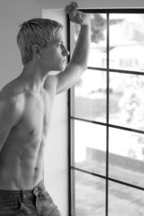 Fototapeta na wymiar Shirtless young man looking out of the window