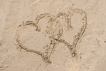 Two entangled hearts drawn out on a sandy beach