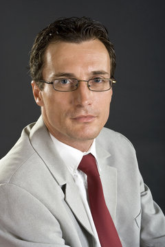 Man in grey jacket with red tie and glasses