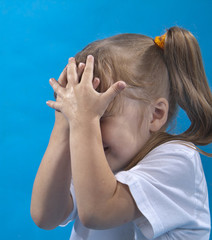 Small girl is covering her face by hands isolated on blue