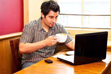 young man using a laptop and drinking cappuccino