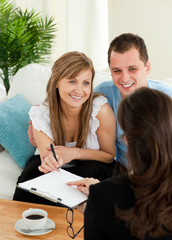 Happy young couple signing a contract sitting in the living room