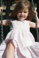 Cheerful little girl swinging, looking away from the camera