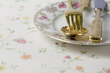 Porzellanteller mit goldenem Besteck auf Blümchentischdecke