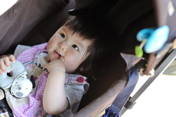 乳母車に横たわり指をくわえる赤ちゃん