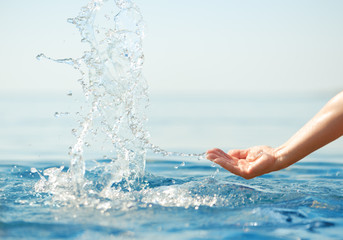 Hand splashing clean water on blue sea background.
