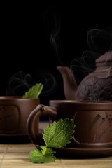 Brown clay asian teapot with sprigs of mint and tea
