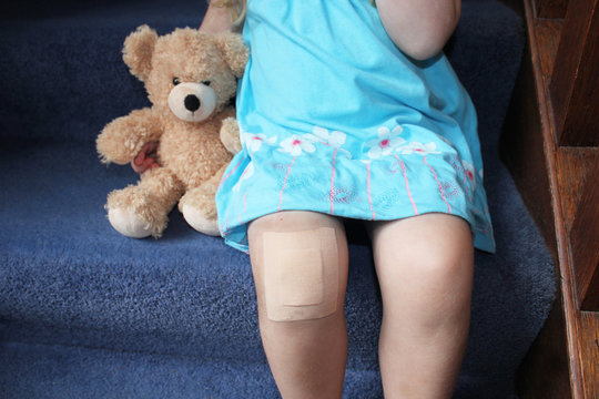girl with plaster on knee cuddling teddy