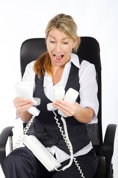 Frazzled Businesswoman Holding Lots Of Telephones In Office