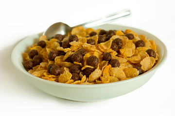 Cornflakes, cocoa balls and spoon in a bowl isolated on white.