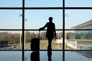Fototapeta premium silhouette of girl with luggage standing in airport