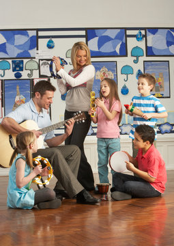 Teachers Playing Guitar With Pupils Having Music Lesson In Class