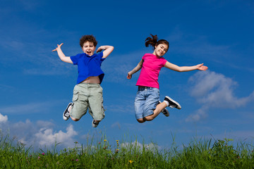 Girl and boy jumping, running against blue sky