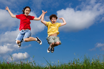 Girl and boy jumping, running against blue sky