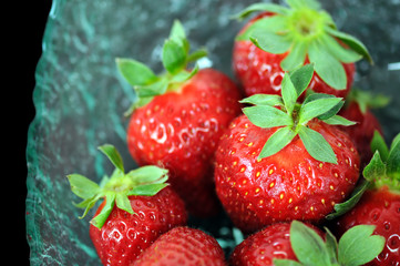 Glass bowl with fresh strawberries on black background.