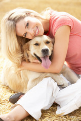 Woman Sitting With Dog On Straw Bales In Harvested Field