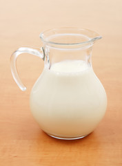 Glass jug full of milk on wooden table