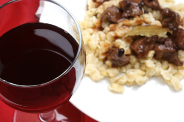 Rotwein im Glas mit Wildgulasch  im Hintergrund