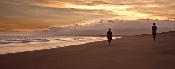 Fototapeta na wymiar Two blurred silhouettes walking on a beautiful beach at sunset