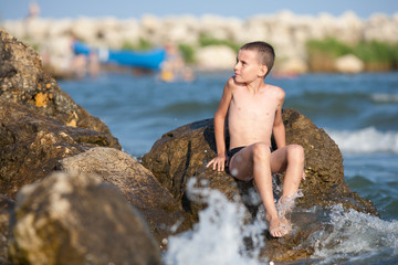 Little boy sitting on rocks at sea