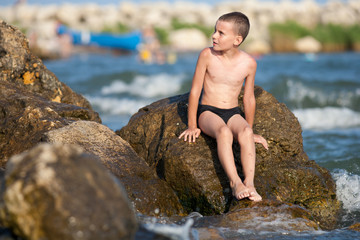 Little boy sitting on rocks at sea