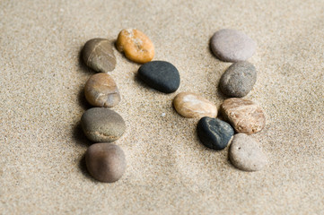 Fototapeta na wymiar lettre N en galets zen dans le sable