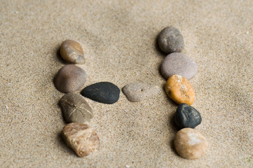 Fototapeta na wymiar lettre H en galets zen dans le sable