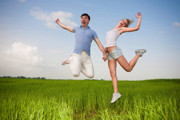 Happy smiling couple  jumping in sky above a green meadow