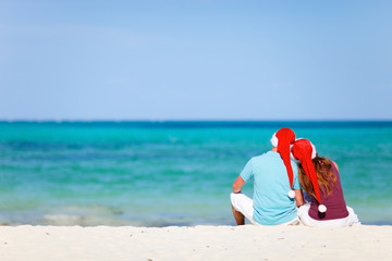 Romantic couple in Santa hats sitting on tropical beach