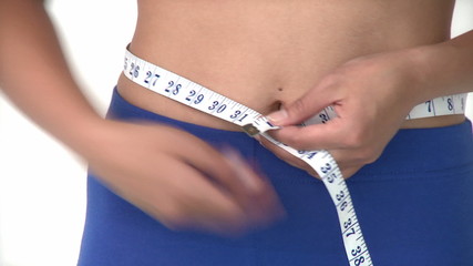 Cute asian woman measuring her waist with a tape measure against - Powered by Adobe