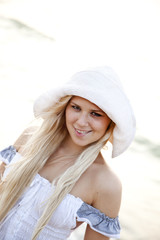 Beautiful young blonde girl in hat on the beach