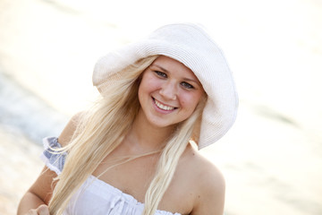 Beautiful young blonde girl in hat on the beach