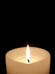 Close up of one lit white candle on black background.