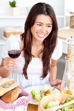 Captivating asian woman holding a wineglass eating a salad at ho