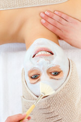 Glowing young woman receiving white cream on her face