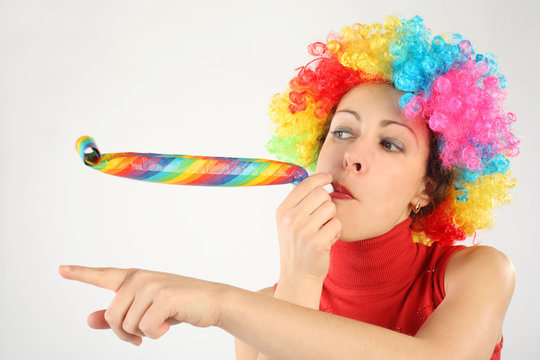 young beauty woman in clown wig and party blower pointing left