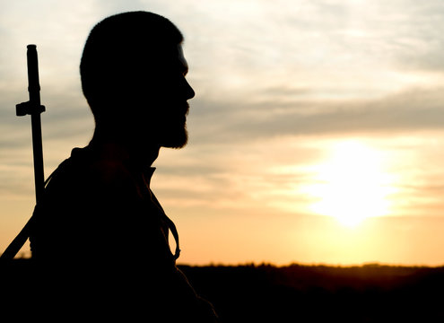 Silhouette of man with rifle during sunset