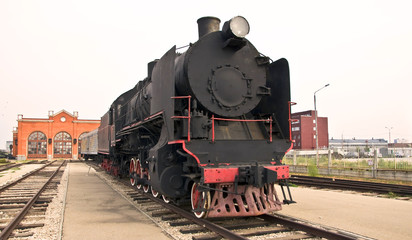 Fototapeta premium Steam locomotive beside a railway station platform. Retro train.