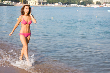 Dark-haired girl in a swimsuit walking on the beach